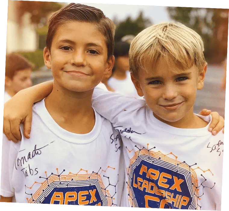 Two smiling elementary students in Apex Leadership shirts with their arms around each other