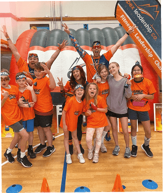 Students in orange Apex shirts cheering with an Apex coach in a school gym