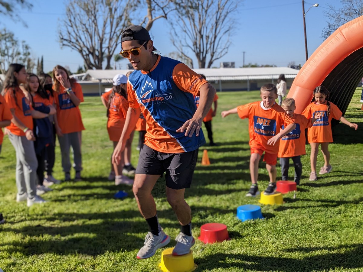 An Apex coach leading students in orange Apex shirts out of the inflatable arch