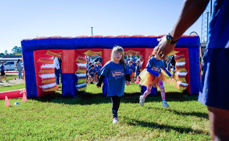 Elementary student running through an inflatable obstacle course as an Apex coach cheers