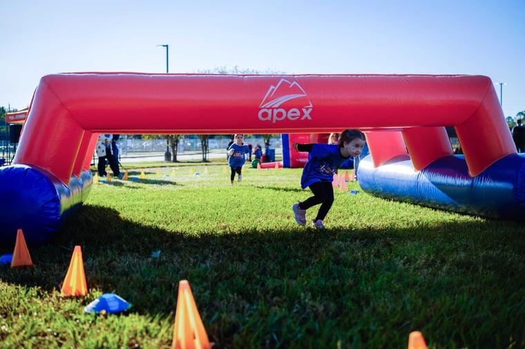 Students racing through a red inflatable obstacle at an Apex obstacle course fundraiser