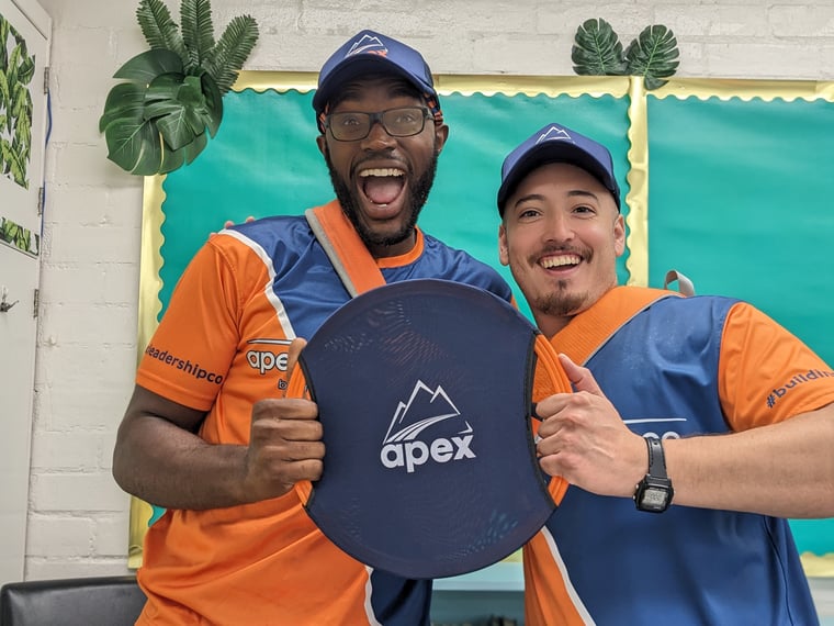 Two cheering Apex coaches holding an Apex frisbee in an elementary classroom