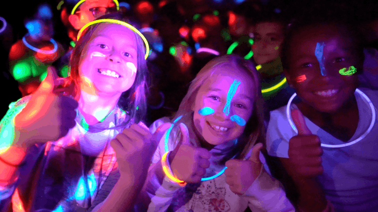 Smiling students with glow sticks and neon face paint at an Apex Remix dance party