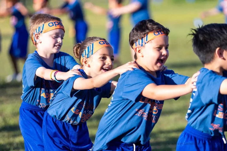 Laughing students in blue Apex shirts and headbands dancing in a line at a fun run