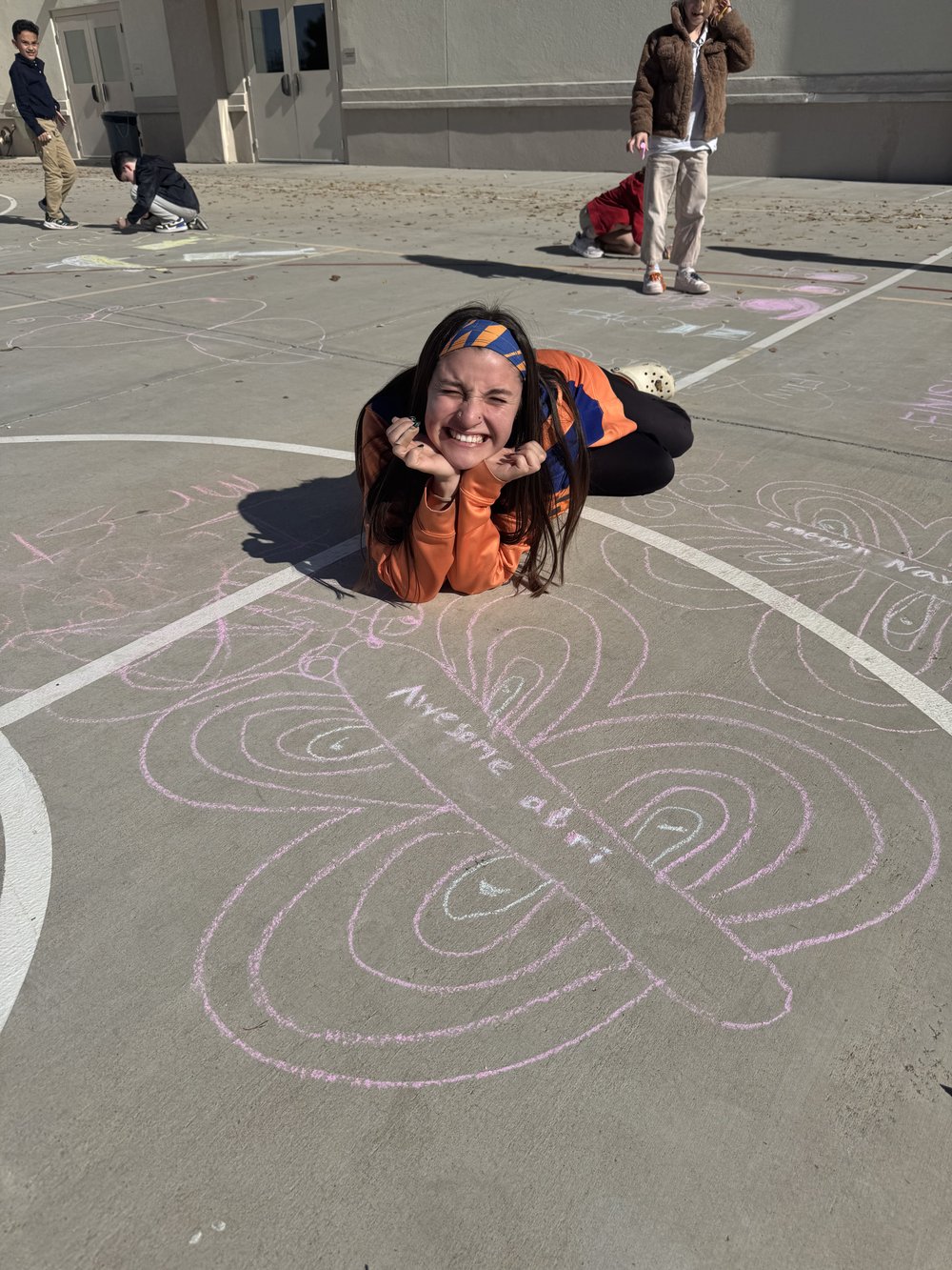Apex coach Awesome Abri smiling next to a chalk butterfly students drew with her name
