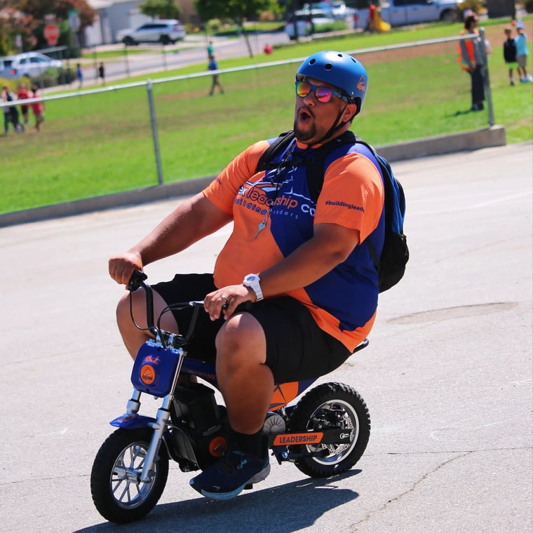 Apex coach riding a mini motorbike in a helmet during a school fundraiser celebration