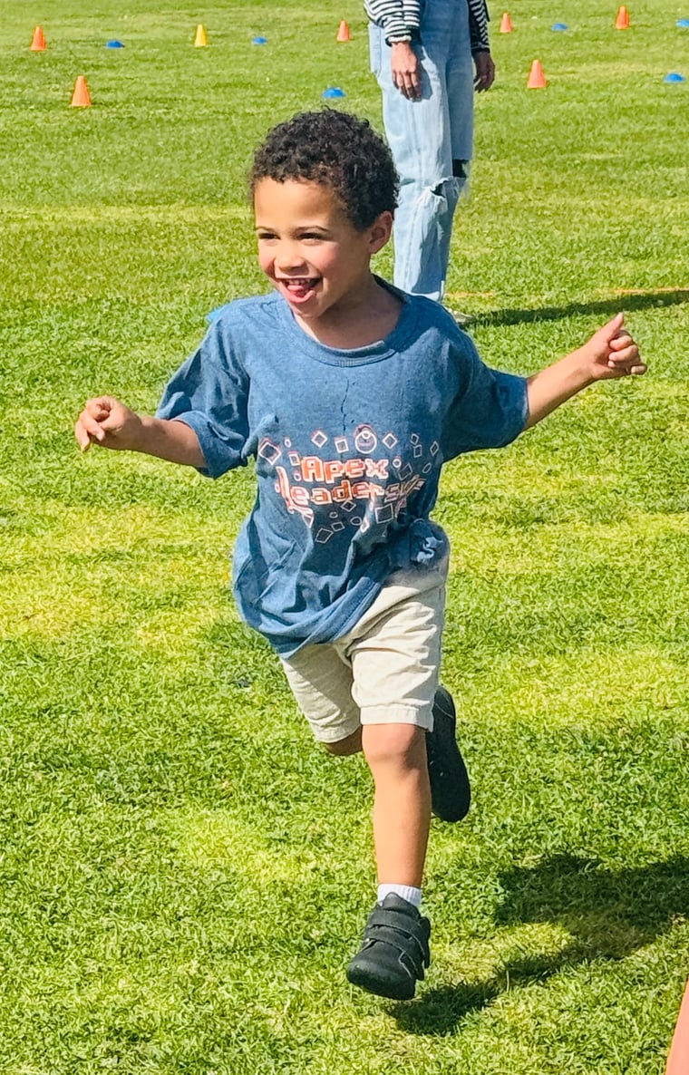 Smiling student in an Apex shirt running across a school field at a fun run