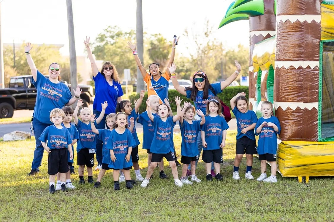 Young students and teachers in Apex shirts cheering in front of an inflatable at a school fun run